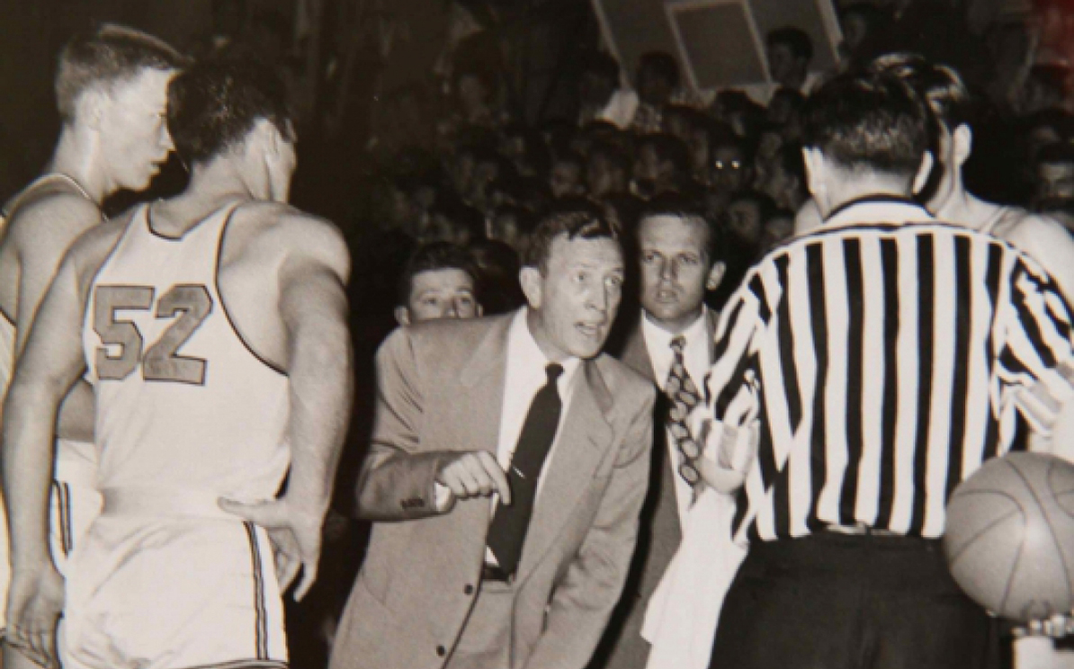 Leans and points at ref in '50